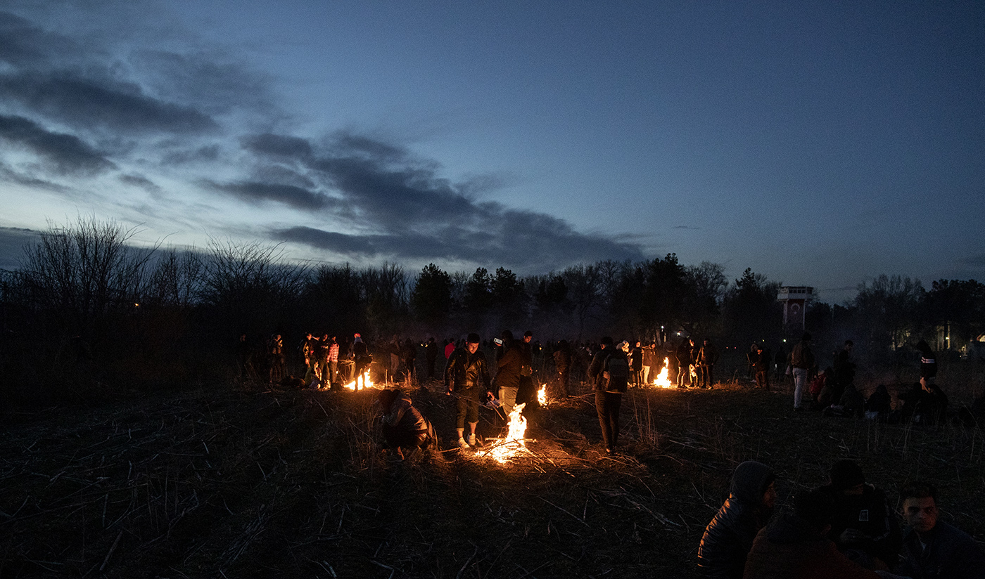 Refugees warm up around a fire near fences enforcing the Greek border as they try to enter Europe, in Edirne, Turkey, 28 February 2020. 