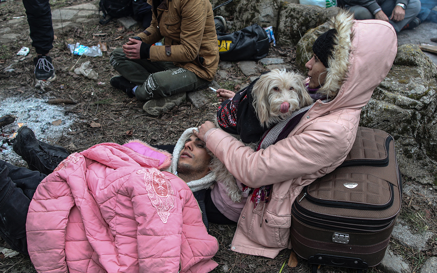 Refugees have some rest before attempting to pass the closed-off Turkish-Greek border and try to enter Europe, Edirne, Turkey, 29 February 2020, while Greek border officials look on from the Greek side.