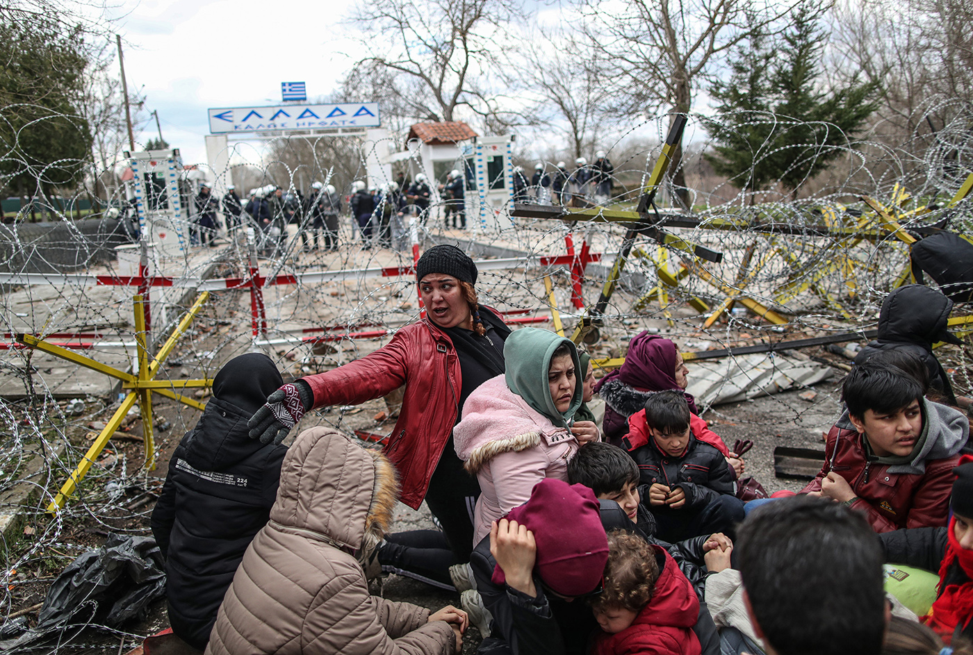 Refugees have some rest before attempting to pass the closed-off Turkish-Greek border and try to enter Europe, Edirne, Turkey, 29 February 2020, while Greek border officials look on from the Greek side. 