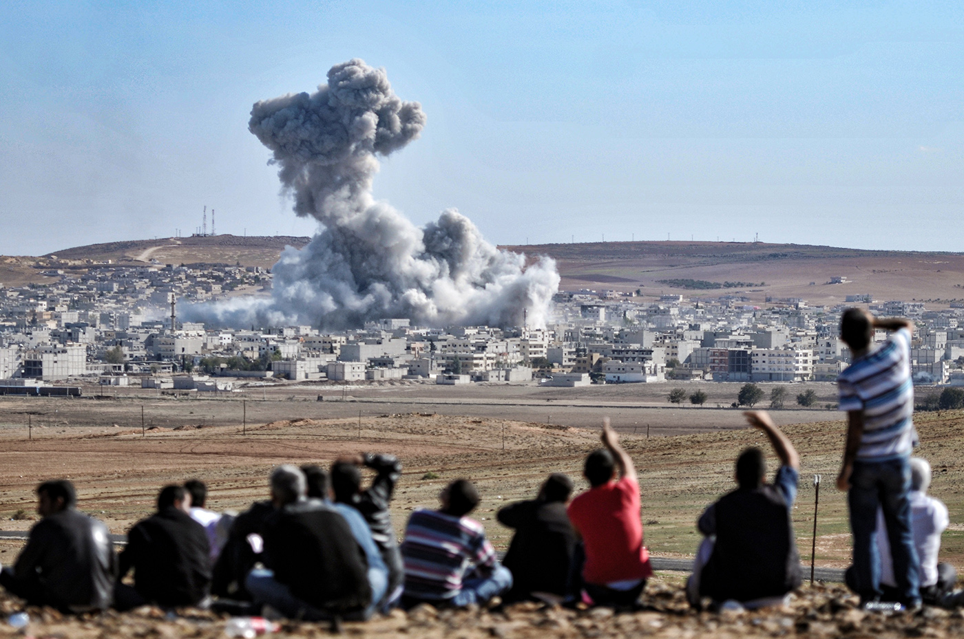 People watch an explosion after an apparent US-led coalition airstrike on Kobane, Syria, as seen from the Turkish side of the border, near Suruc district, Sanliurfa, Turkey, 22 October 2014.