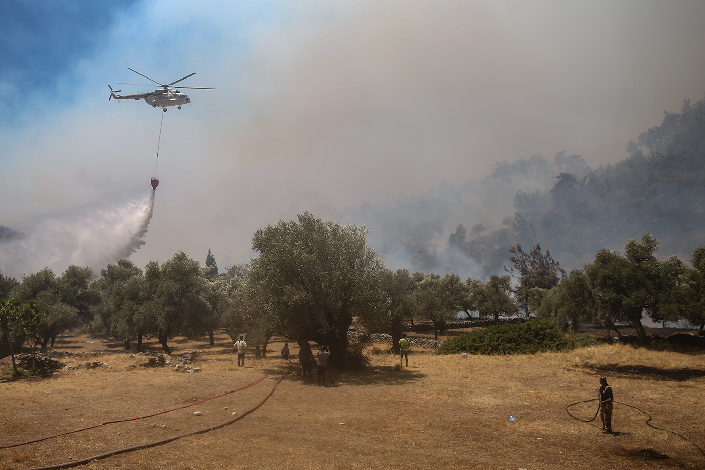 A helicopter waterbombs a wildfire burning at the Cokertme village of Milas district of Mugla, Turkey, 02 August 2021. Turkish Health minister Fahrettin Koca confirmed that eight people have lost their lives due to the wildfires raging in Turkey’s Mediterranean towns.