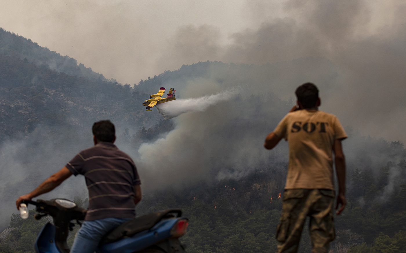 Spanish hydroplanes waterbombs a wildfire burning as people watch near the Yuvarlakcay village of Koycegiz district of Mugla, Turkey, 04 August 2021. Turkish Health minister Fahrettin Koca confirmed that eight people have lost their lives due to the wildfires raging in Turkey’s Mediterranean towns.