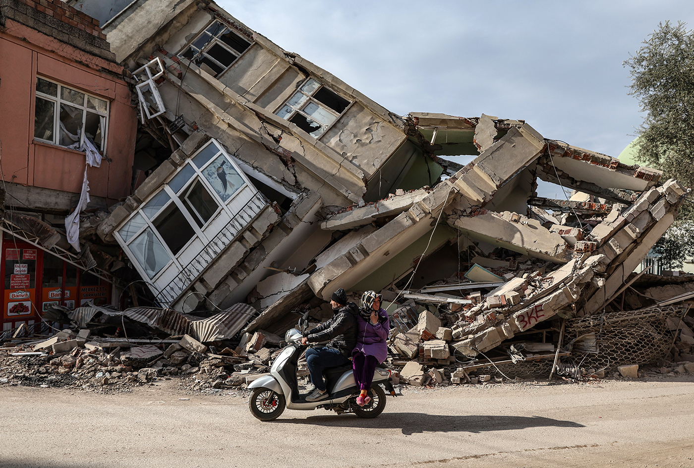 People pass by a motorcyle in front of a collepsed building after powerful earthquake in Adiyaman, Turkey, 19 February 2023. More than 45,000 people have died and thousands more are injured after two major earthquakes struck southern Turkey and northern Syria on 06 February. Authorities fear the death toll will keep climbing as rescuers look for survivors across the region.